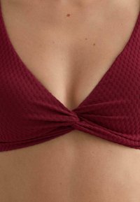 Bordowy top bikini z teksturowanym, prążkowanym wzorem, z ozdobnym skręceniem z przodu i trójkątnym kształtem.