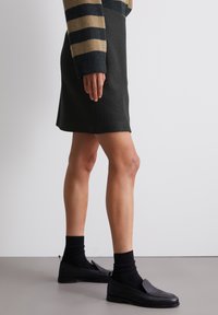 Mini gonna in misto lana nera abbinata a scarpe slip-on in pelle nera e calzini in maglia neri, mostrata di lato per una vista dettagliata.