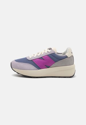 Lavprofilsneaker i blåt mesh og gråt ruskind med en tyk hvid sål og en fremtrædende lilla "N" logo på siden.
