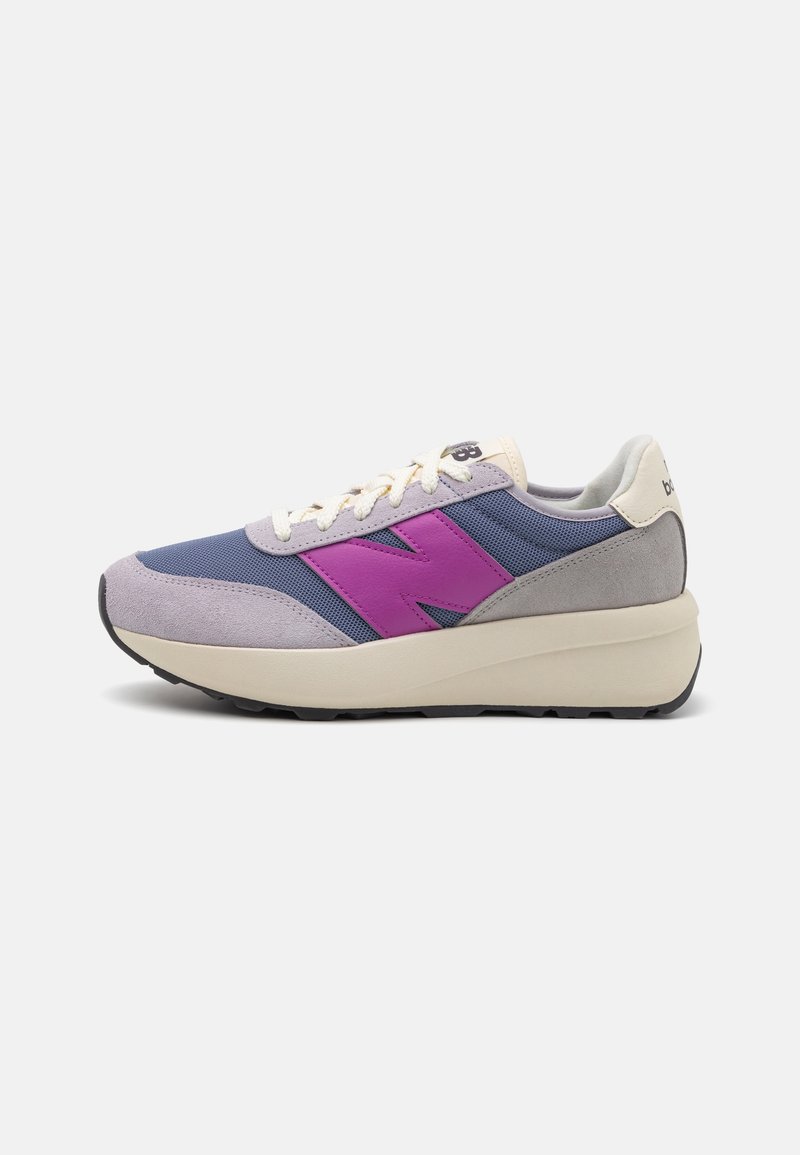 Baskets basses en mesh bleu et daim gris avec une semelle blanche épaisse et un logo violet "N" bien visible sur le côté.
