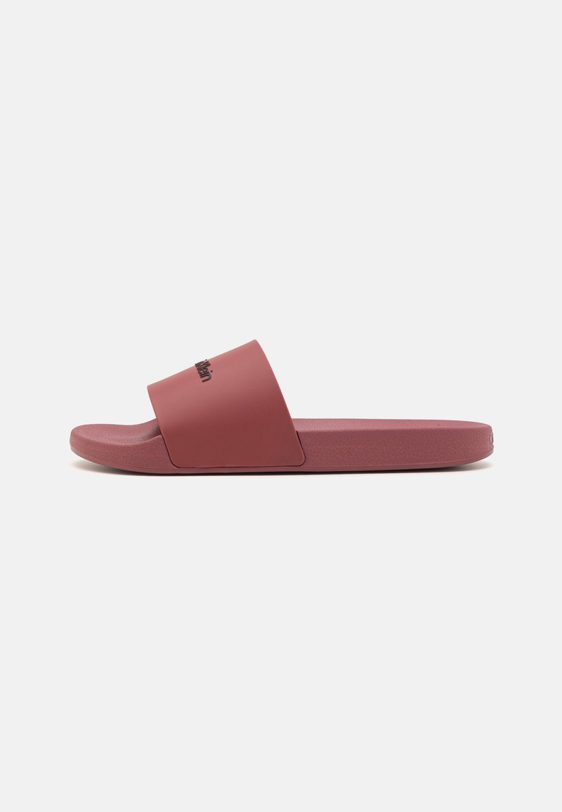 Sandale roșii cu toc plat, cu o curea lată, fabricate din material de cauciuc neted. Sole plată cu un finisaj texturat și un logo imprimat pe curea superioară.