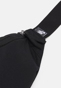 Svart tygpåse med dragkedja, försedd med ett robust bälte och en liten Nike-logotag. Texturerad yta för bättre grepp.
