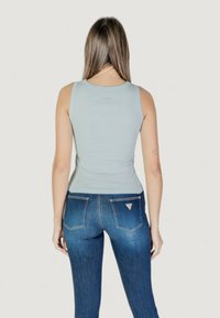 Top senza maniche di un azzurro chiaro con un design aderente, realizzato in tessuto morbido, abbinato a jeans blu scuro con un'etichetta triangolare del marchio sulla tasca posteriore.