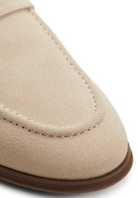 Primer plano de la puntera de un zapato de ante beige con costuras detalladas y borde de suela de goma marrón.