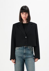 Skuren svart kavaj i slät tyg med enknappslåsning och smala, långa �ärmar. Bärs över en ribbad svart topp och denimjeans.