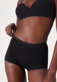 Black cotton briefs with a smooth texture, featuring a wide elastic waistband. The design is fitted and offers full coverage.