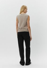 Bež bezrukavni top napravljen od mekanog materijala, uparen s crnim hlačama širokih nogavica. Jednostavan dizajn bez vidljivih uzoraka ili naglasaka.