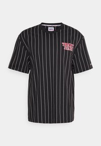 Černé tričko s krátkým rukávem a bílými svislými pruhy. Na levé straně se nachází červené logo "TOMMY JEANS". Vyrobeno z bavlněné tkaniny.