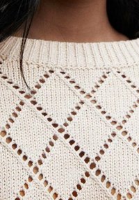 Pull en maille couleur crème présentant un motif en losange avec des détails ajourés, un col rond côtelé et un tissu texturé.