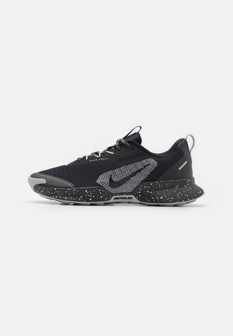 Chaussure de trail Nike noire et grise, semelle tachetée, empeigne texturée et grand swoosh Nike sur le côté.
