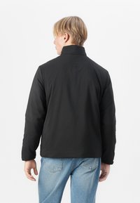 Svart polstret jakke med høy krage, glatt tekstur og lange ermer, kombinert med lyseblå denimjeans.