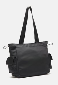 Black nylon tote bag with two side pockets, top zip closure, and long straps for carrying. Smooth texture and minimalistic design.