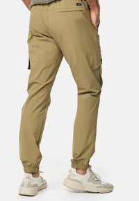 Khaki cargo bukser med elastiske manchetter, sidelommer og detalje på baglommen. Båret med hvide og beige sneakers. Glat stof tekstur.