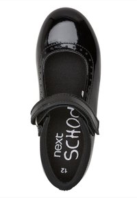 Scarpa in pelle verniciata nera con punta arrotondata, cinturino regolabile e soletta testurizzata con branding bianco. Superficie liscia e lucida.
