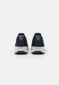 Navy blue athletic shoes with a knit upper, featuring a contrasting white sole, textured panels, and a logo patch on the heel.