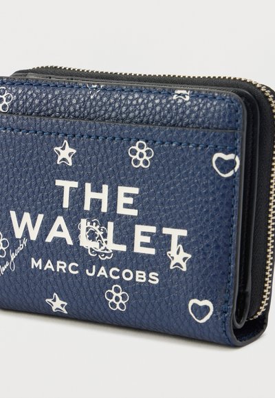 Marineblåt tekstureret læderpung med hvide trykte stjerner og blomster, lynlås, og præget logo "THE WALLET MARC JACOBS."