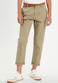 Chinos kaki à coupe ample, avec des manches retroussées et une ceinture tressée marron. Associés à des baskets blanches avec des accents beiges et un design texturé.
