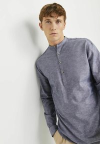 Camicia henley a maniche lunghe con bottoni, realizzata in un tessuto blu scuro testurizzato. Caratterizzata da un colletto arrotondato con una placca a tre bottoni.