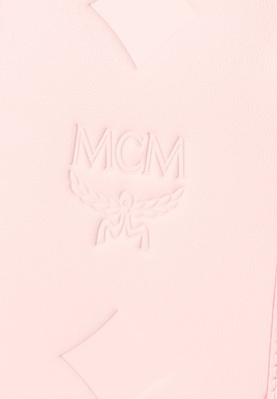 Ανεβασμένο λογότυπο MCM με φιγούρα με φτερά σε φόντο από ροζ δερμάτινη επιφάνεια με υφή.