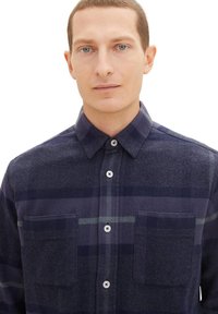 Koszula flanelowa w marynarską kratę, z dwiema przednimi kieszeniami, zapinana na guziki, w kontrastowych odcieniach niebieskiego i zieleni. Klasyczny kołnierzyk i detale z guzikami.