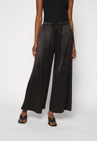 Svarta satinbyxor med vida ben, resårmidja och dragsko. Slät textur och hel längd. Bärs med svarta glidsandaler.