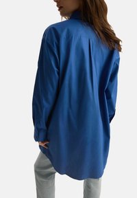 Niebieska, koszula z długim rękawem i guzikiem, luźny krój, z plisą z tyłu i mankietami, wykonana z gładkiego materiału.