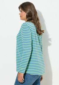 Sinivihreäraidsinen pitkähiha-paita, rento istuvuus, sivuhalkiot ja pieni rannelogo. Yhdistetty sinisiin farkkuihin.