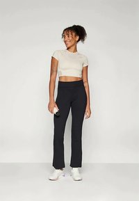 Top corto beige y leggings de campana negros hechos de un tejido elástico, combinados con zapatillas blancas. La modelo sostiene una botella de agua pequeña.