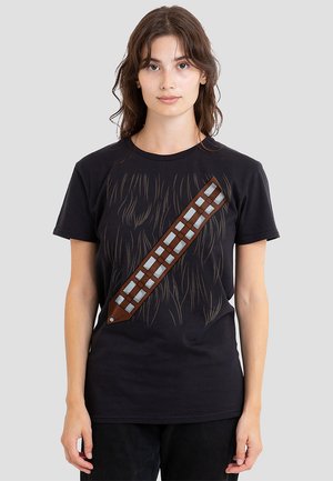 Schwarzes T-Shirt mit einem Grafikmotiv von braunem Fell und einem braunen Bandolier-Design über der Vorderseite, verziert mit silbernen rechteckigen Akzenten.