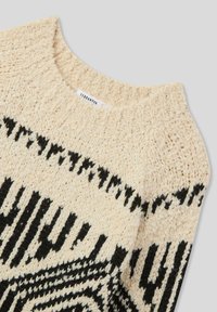 Maglione lavorato a maglia in crema con motivi geometrici neri. Presenta una scollatura rotonda e un tessuto strutturato per un aspetto accogliente.