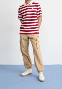 Randig polo-tröja i rött och vitt med krage, beige cargobyxor och vita sneakers med gummisulor. Enkelt mönster, avslappnad passform och lättviktsmaterial.