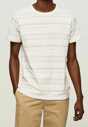 Baumwoll-T-Shirt mit Rundhalsausschnitt, das horizontale beige Streifen auf einem off-weißen Hintergrund zeigt. Kurze Ärmel und ein gerader Saum. Rotes Etikett an der Seite.