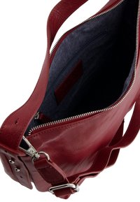 Red læder skuldertaske med sølvzipper åben, som viser mørkt stofinteriør og lynlåslomme indeni.