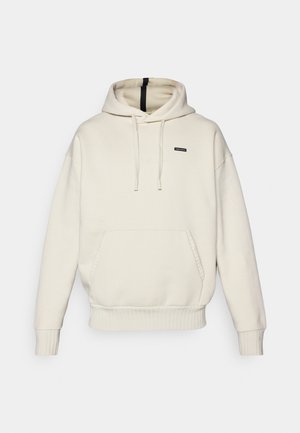 Hoodie beige clair avec une poche kangourou, des poignets et un ourlet côtelés, une capuche avec cordon de serrage, et une petite étiquette de marque noire sur la poitrine.
