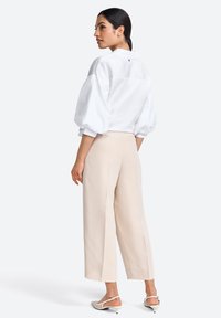 White, oversized, long-sleeve shirt with puffed sleeves, worn with beige wide-leg trousers and white heeled sandals.