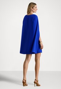 Kék köpönyszerű ruha bő szabással, kerek nyakkivágással és légies anyaggal. Barna magas sarkú szandállal párosítva.