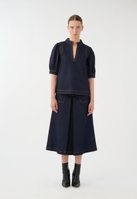 Dunkelblaue Jeansbluse mit Puffärmeln und einem Schlüsselloch-Ausschnitt; kombiniert mit einem passenden Rock mit einem Schlitz vorne und kontrastierenden Nähten.