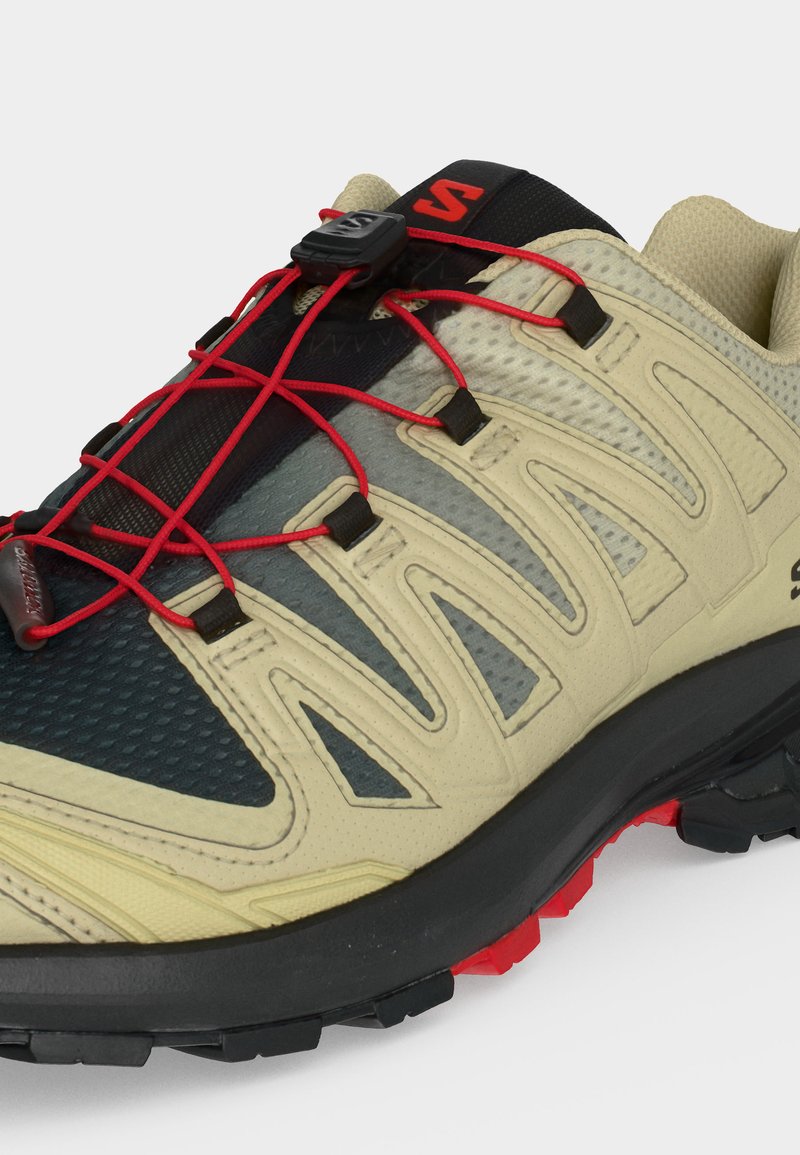 Chaussure de randonnée beige et noire avec système de laçage rapide rouge et semelle extérieure noire avec accents rouges sur la bande de roulement.