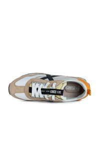 Zapatilla beige y blanca con un acento negro, materiales de ante y malla, cordones blancos, lengüeta trasera naranja y etiqueta de marca en la lengüeta.
