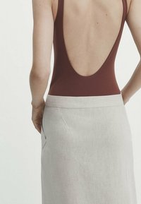 Bruin rugloos badpak gecombineerd met een lichtgrijze linnen rok met een sluitende taille en zijzakdetails. Glad textuur en minimalistisch ontwerp.
