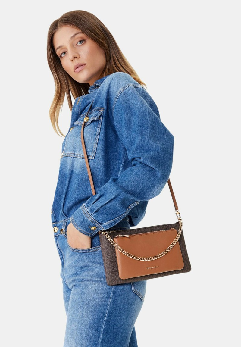 Sac bandoulière marron à motifs avec un accent chaîne, comprenant une poche zippée, porté avec une tenue en denim ornée de boutons.