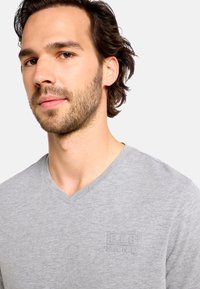 Sivé tričko s výstrihom do V vyrobené z jemnej látky, s decentným reliéfnym logom na hrudi. Minimalistický dizajn s hladkou textúrou.