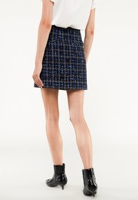 Kort blå och svart tweedkjol med figursydd midja, texturerad tyg och rak passform, tillsammans med blanka svarta anklarstövlar.