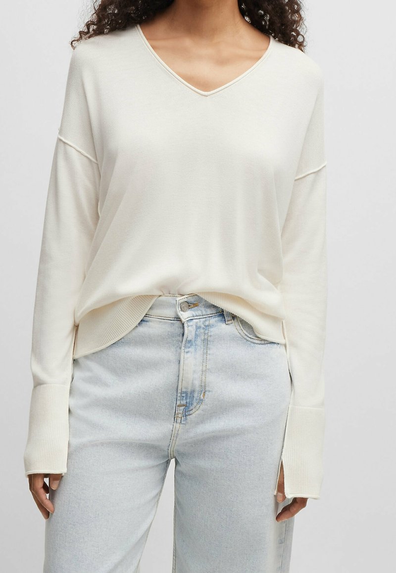 Frau in einem lockeren, cremefarbenen V-Ausschnitt-Pullover mit langen Ärmeln und hellblauen High-Waist-Jeans.