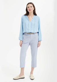 Blusa azzurro chiaro a maniche lunghe con bottoni frontali e motivo testurizzato, abbinata a pantaloni cropped grigi chiari e mocassini beige.