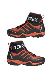 Chaussures de randonnée montantes en noir et orange vif, présentant une surface texturée, un design à lacets et trois rayures noires sur le côté.