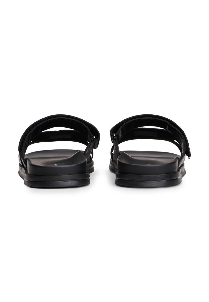 Sandalias negras con dos tiras anchas, una suela plana y un diseño minimalista. El material parece ser sintético con una textura suave.