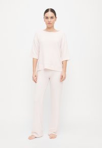 Σετ λευκής ρόμπας σε ανοιχτό ροζ χρώμα που περιλαμβάνει ένα άνετο τοπ με κοντά μανίκια και ψηλό λαιμό, συνδυασμένο με ταιριαστά tapered παντελόνια. Μαλακή υφή.