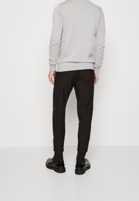 Sweat-shirt gris clair à manches longues, associé à un pantalon noir fuselé. Le pantalon présente une texture lisse et arrive à la cheville. Des chaussures noires à finition brillante complètent le look.