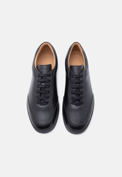 Μαύρα αθλητικά παπούτσια από δέρμα με κορδόνια, με ταμπά εσωτερική επένδυση, φωτογραφημένα από ψηλά πάνω σε λευκό απλό φόντο.